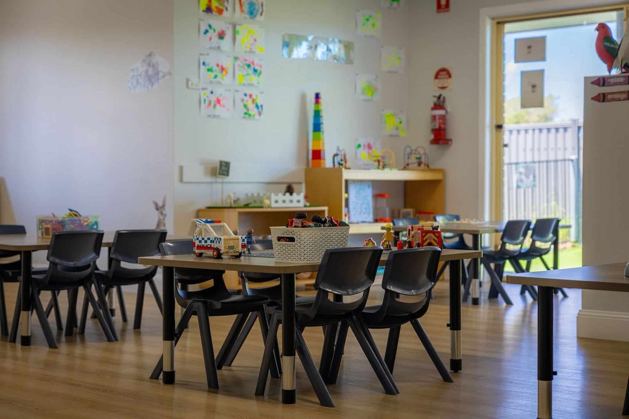 A Cherubs Academy classroom: child-sized tables set with toy vehicles, children’s paintings on the walls, and the yard through an open door