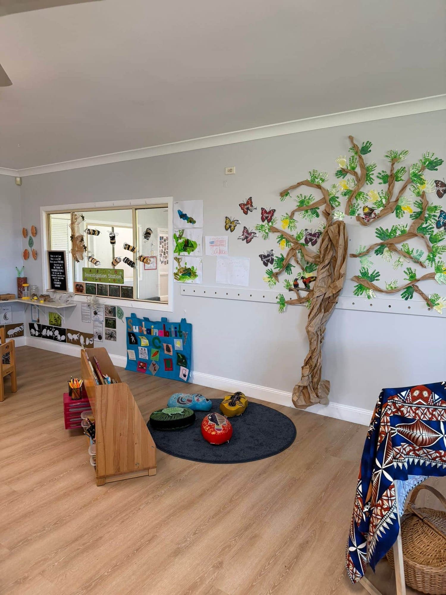 Quiet reading nook with cushions and baskets beside the tree mural