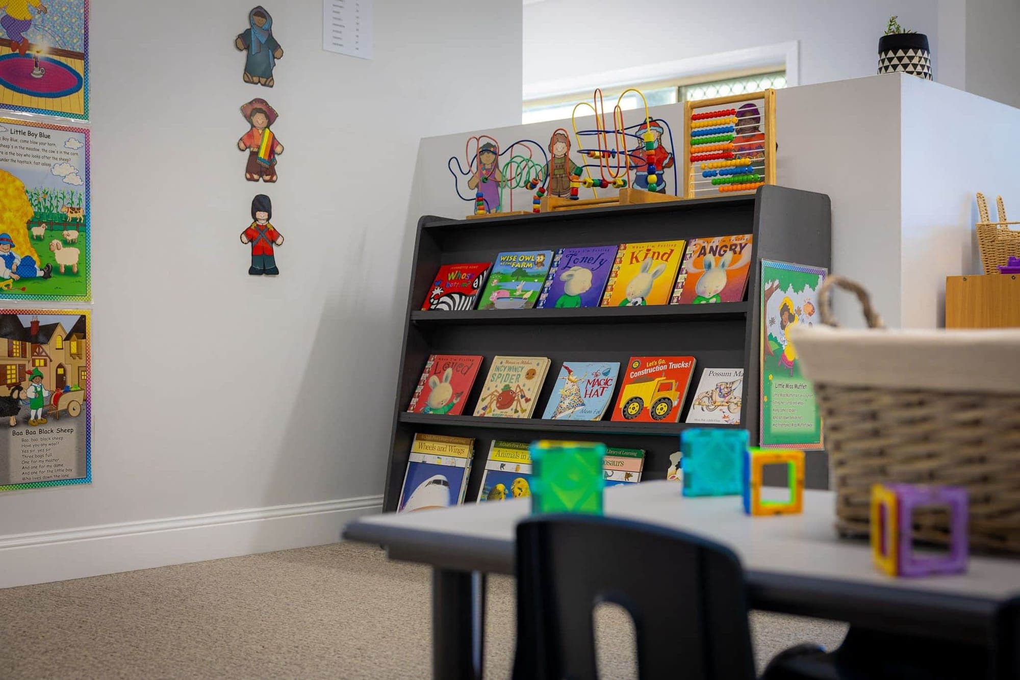 Picture books displayed on a low shelf beside a basket of blocks